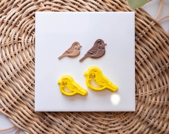 May include: Four bird-shaped cookie cutters on a white surface. Two are brown and two are yellow.