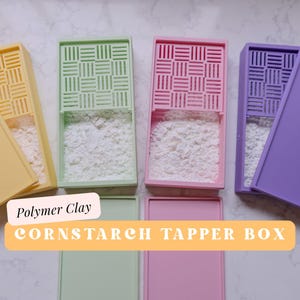 Puede incluir: Cinco cajas de plástico de colores con tapas, etiquetadas "Polymer Clay Cornstarch Tapper Box". Cada caja tiene un patrón de cuadrícula en la parte superior y está llena de polvo blanco.
