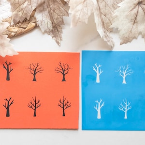 May include: Two cards featuring tree designs. One is orange with black tree illustrations, the other is blue with white tree illustrations. The blue card has the text "ECHO STONE". Dried leaves are in the background.