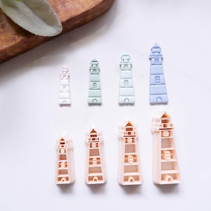 Puede incluir: Una colección de objetos con forma de faro en varios tamaños y colores. Los faros varían de rosa claro a azul claro. La imagen está tomada desde arriba, con los faros dispuestos sobre una superficie blanca.