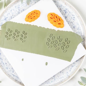 Może przedstawiać: Zbliżenie na białą powierzchnię z dwoma pomarańczowymi stemplami w kształcie liści i zieloną powierzchnią z gliny z dwoma wytłoczonymi wzorami liści.