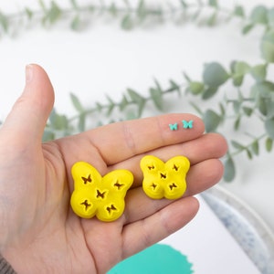 Puede incluir: Dos moldes de silicona en forma de mariposa de color amarillo con recortes de mariposa más pequeños. También se muestran dos moldes de mariposa turquesa más pequeños.
