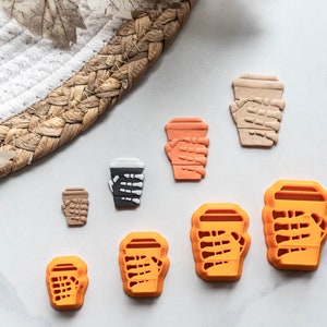 May include: Set of seven orange and brown cookie cutters shaped like coffee cups with skeleton hands holding them.
