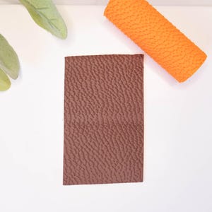 May include: A brown textured faux leather sheet. The sheet is rectangular and has a slightly rough surface.