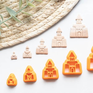 May include: A set of nine sandcastle cookie cutters in various sizes. The cutters are made of plastic and are in shades of orange and beige.