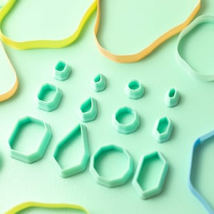 May include: A set of 11 turquoise blue cookie cutters in various geometric shapes, including circles, diamonds, and rectangles, on a light green background.