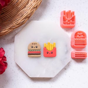 Puede incluir: Un juego de cuatro moldes de silicona rosa para hacer encantos de arcilla polimérica con temática de comida. Los moldes presentan una hamburguesa, papas fritas y dos estilos diferentes de papas fritas.
