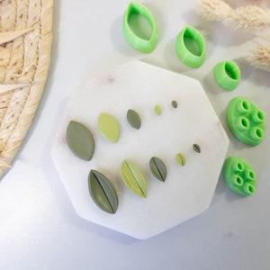 May include: A white hexagonal tray with green polymer clay leaf shapes and a green polymer clay mold with multiple circles. The tray is on a white surface.