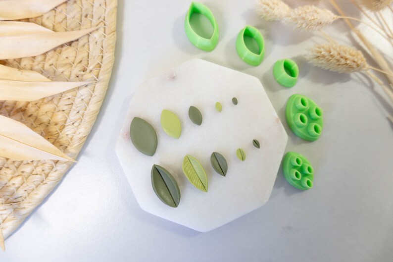 May include: A white hexagonal tray with green polymer clay leaf shapes and a green polymer clay mold with multiple circles. The tray is on a white surface.