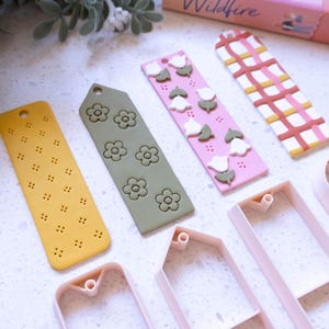 Op de afbeelding: Vijf verschillende polymer clay-bladwijzers met verschillende patronen en ontwerpen. De bladwijzers zijn in tinten roze, geel, groen en bruin. Er zijn ook vijf roze plastic uitstekers voor het maken van de bladwijzers.