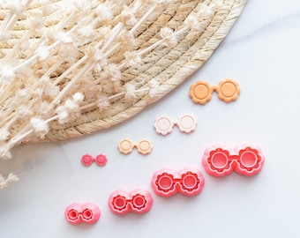 May include: A set of six pink and orange plastic cookie cutters shaped like sunglasses. The cutters are arranged in a row on a white surface.