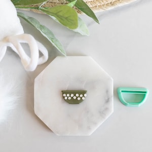 May include: A green ceramic bowl with white flower accents and a green plastic bowl cutter on a white marble surface.