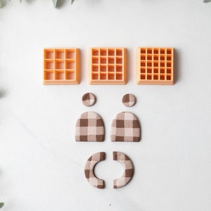 Può includere: Tre stampi per waffle in plastica arancione, due forme ad arco a scacchi marroni e bianchi e due cerchi a scacchi marroni e bianchi.