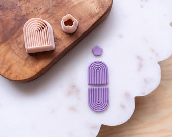Puede incluir: Un juego de cortadores de galletas de silicona de color morado y rosa en forma de arcoíris. Los cortadores están sobre una superficie de mármol blanco.