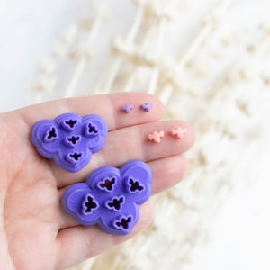May include: Two purple silicone molds shaped like clouds with multiple flower-shaped cutouts. Two smaller pink silicone molds shaped like flowers.