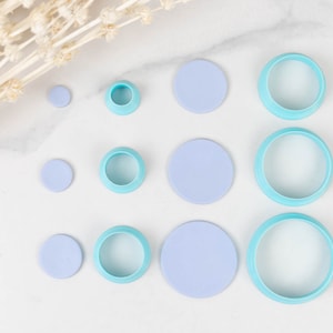 May include: A set of nine round cake cutters in various sizes. The cutters are light blue and made of plastic. They are arranged in three rows on a white surface.