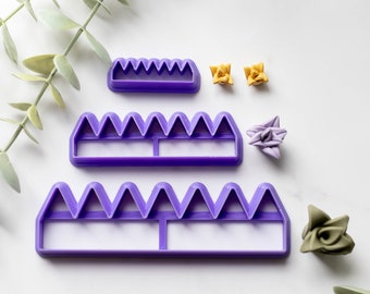 May include: Three purple plastic cake decorating tools with different sized scalloped edges. The tools are arranged in a pyramid shape on a white surface. There are also four small origami flowers in yellow and purple.
