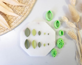 May include: A set of green plastic leaf-shaped cookie cutters on a white marble surface. The cutters are arranged in rows of different sizes.
