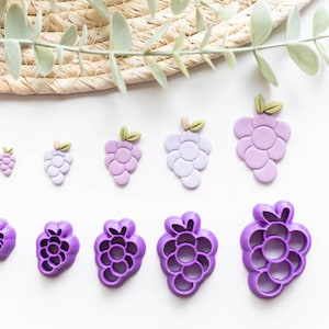 May include: A set of eight purple grape-shaped cookie cutters in various sizes. The cutters are made of plastic and have a smooth, shiny finish.
