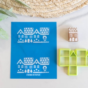 Könnte beinhalten: Eine blaue Schablone mit zwei Lebkuchenhaus-Designs und dem Text "Echo Stone". Außerdem gibt es ein braunes Lebkuchenhaus und eine grüne Lebkuchenhaus-Form aus Kunststoff.