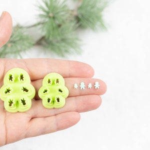 May include: Two green plastic cookie cutters shaped like a gingerbread person, with smaller versions of the cutter in a row on a finger.