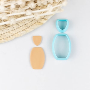 May include: A set of three blue plastic cookie cutters shaped like a bottle, a bottle top, and a small oval. The cutters are on a white surface next to two brown fondant shapes.