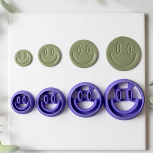 May include: Set of six smiley face cookie cutters in two sizes and two colors. The smaller cutters are purple and the larger cutters are green.