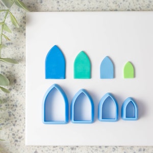 May include: A set of seven blue and green plastic cookie cutters shaped like arched windows. The cutters are arranged in two rows, with the larger cutters in the back and the smaller cutters in the front.
