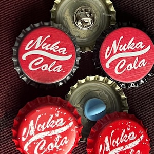 May include: Five red bottle caps with the words "Nuka Cola" printed in white. The bottle caps are arranged in a circle with the words facing outwards.