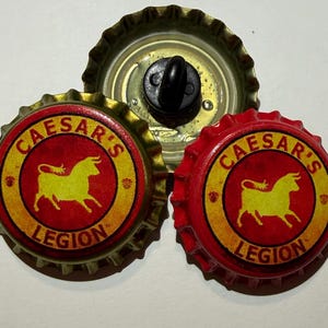 May include: Three bottle cap magnets. Two are red and gold with the text "CAESAR'S LEGION" and a yellow bull graphic. The third is a gold bottle cap with a black magnet attached.
