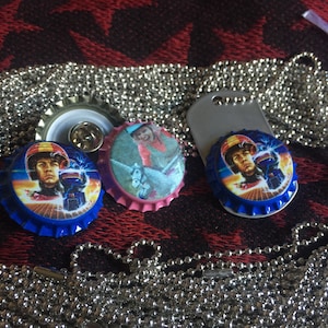 May include: Three bottle cap charms featuring images of characters from the movie Back to the Future. The charms are attached to a silver chain necklace.