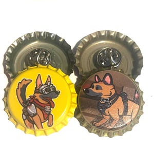 May include: Two bottle cap pins with cartoon German Shepherd designs. One has a yellow background and the dog wears goggles and a red scarf. The other has a brown background and the dog wears a harness.