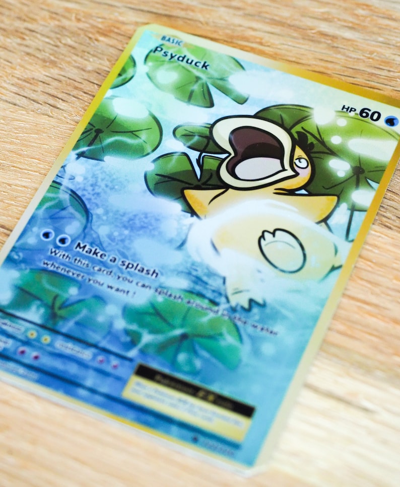 May include: A Pokemon trading card featuring Psyduck, a water-type Pokemon. The card is a basic card with a gold border and a blue background. The card features an illustration of Psyduck with its mouth open, surrounded by water and lily pads. The card text reads 'Make a splash' and 'With this card, you can splash whenever you want!' The card has a HP of 60.