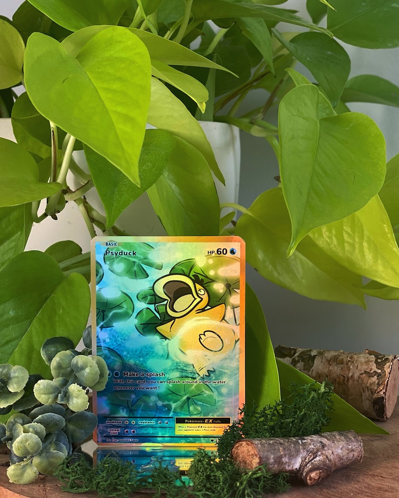May include: A holographic Pokemon card featuring Psyduck. The card is a basic card with a HP of 60. Psyduck is a yellow duck with a green head and a wide open mouth. The card has a blue, green, and yellow background with a holographic effect. The card text reads 'Make a splash. With this card, you can splash around in the water whenever you want!'.