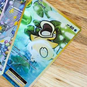 May include: A Pokemon trading card featuring Psyduck, a water-type Pokemon. The card is gold with a blue and green background. Psyduck is depicted with its mouth open and surrounded by lily pads. The card has a HP of 60 and the text 'BASIC Psyduck' is printed in the top left corner. The text 'splash you can splash around in the water 'ant!' is printed in the bottom left corner. The card also has the text 'Pokémon-EX rule' and 'EX' printed in the bottom left corner. The card number '222/220' is printed in the bottom right corner.