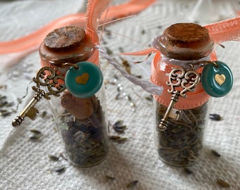 May include: Two small glass bottles with cork tops, filled with dried herbs and tied with peach-coloured ribbon. Each bottle has a silver key charm and a turquoise heart charm.