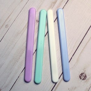 May include: Four nail files in different pastel colors: lavender, light blue, white, and light blue. The files are arranged in a row on a light wood surface.
