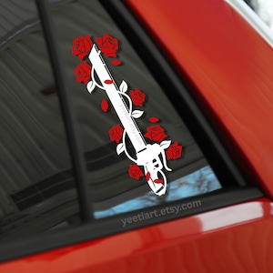 May include: White decal of a sword entwined with red roses and leaves, applied to a car window. The design includes the text "yeetiart.etsy.com". The decal is set against a red car body.