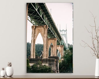 Könnte beinhalten: Fotografie einer Brücke mit gewölbten Stützen und einer grünen Metallkonstruktion darüber. Die Brücke vor einem bewölkten Himmel, mit Bäumen im Hintergrund. Das Bild wird auf einem Regal mit dekorativen Ananas und einer Vase angezeigt.