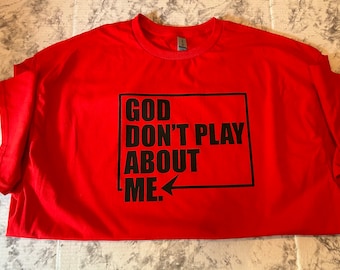 May include: Red t-shirt with black text that reads "GOD DON'T PLAY ABOUT ME."  The text is in a black box with an arrow pointing to the right.