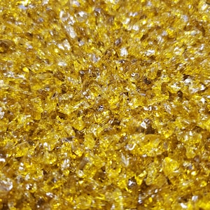 Könnte beinhalten: Nahaufnahme einer großen Menge kleiner, goldgelber Glasstücke. Die Stücke sind unregelmäßig geformt und haben eine leicht durchscheinende Optik.