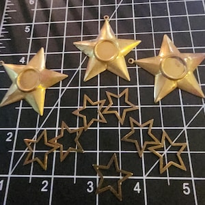 May include: A set of seven gold-toned metal star shapes, some with a circular cutout in the center. The stars are arranged on a black and white grid.