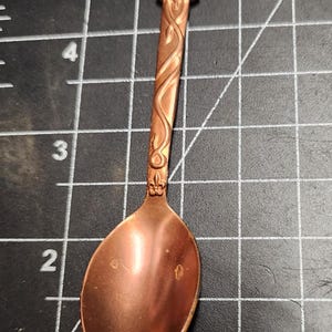 Peut inclure: Une cuillère en cuivre avec un manche décoratif et un bol arrondi. Le manche présente un motif de bouclier surmonté d'une couronne.