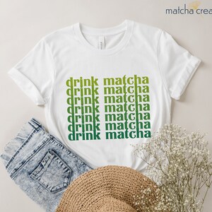 May include: White t-shirt with the text "drink matcha" repeated in a gradient of green and yellow.