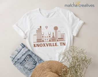 May include: White t-shirt with a brown outline of the Knoxville, TN skyline and the text "KNOXVILLE, TN".