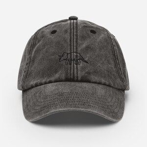 May include: A black vintage style baseball cap with a black embroidered outline of a triceratops dinosaur.
