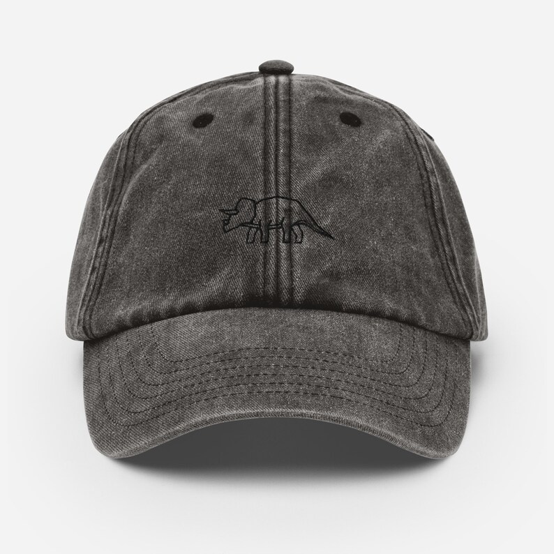 May include: A black vintage style baseball cap with a black embroidered outline of a triceratops dinosaur.