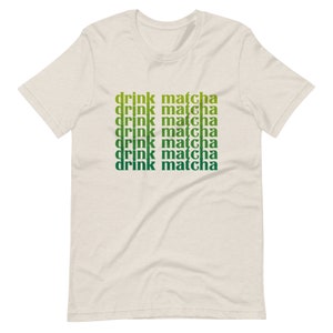 May include: A beige t-shirt with the text "drink matcha" repeated six times in a gradient of green and yellow.