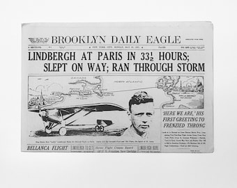 Może przedstawiać: Czarno-biały wycinek z gazety Brooklyn Daily Eagle z 22 maja 1927 roku, z nagłówkiem "LINDBERGH W PARYŻU W 33 1/2 GODZINY; SPAŁ W TRAKCIE PODRÓŻY; PRZEBYŁ BURZĘ". Artykuł opisuje historyczny transatlantycki lot Charlesa Lindberga, w tym mapę jego trasy i zdjęcie Lindberga.