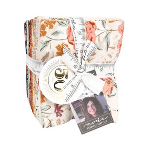 May include: A bundle of floral fabric squares tied with a white ribbon printed with measurements and the "moda FABRICS + SUPPLIES" logo. The fabric features a cream background with peach and brown floral patterns. A tag with a woman's photo is attached.